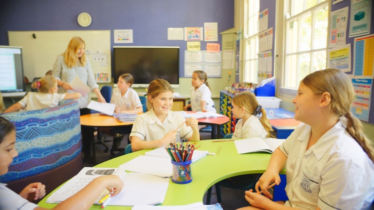 Students learning and smiling in class with teacher in background