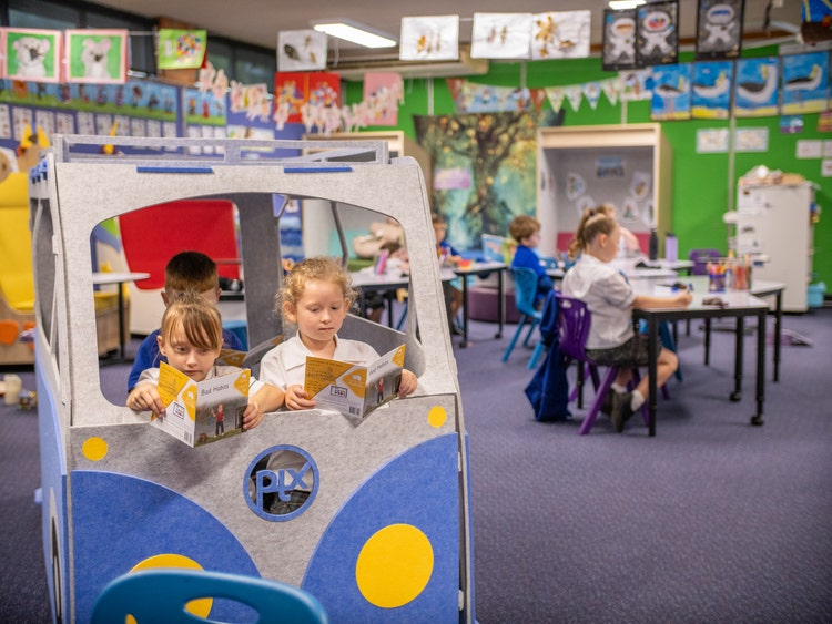 Kindergarten students reading a book in combi and children working in background