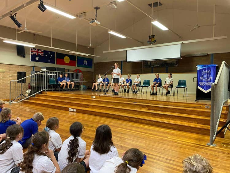 Student standing doing speech for public speaking in hall with whole school